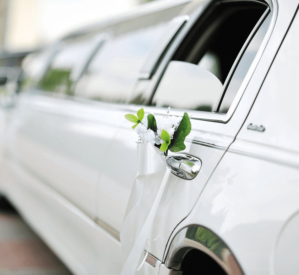 White limousine with a floral arrangement attached to the rear door handle.