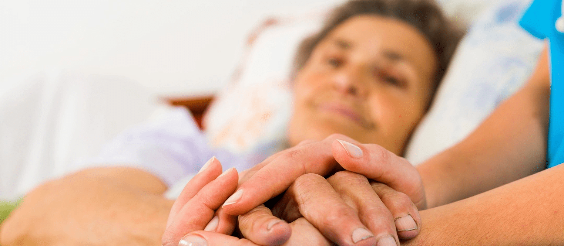 A person in a bed is holding hands with someone in a blue sleeve, conveying comfort and care.